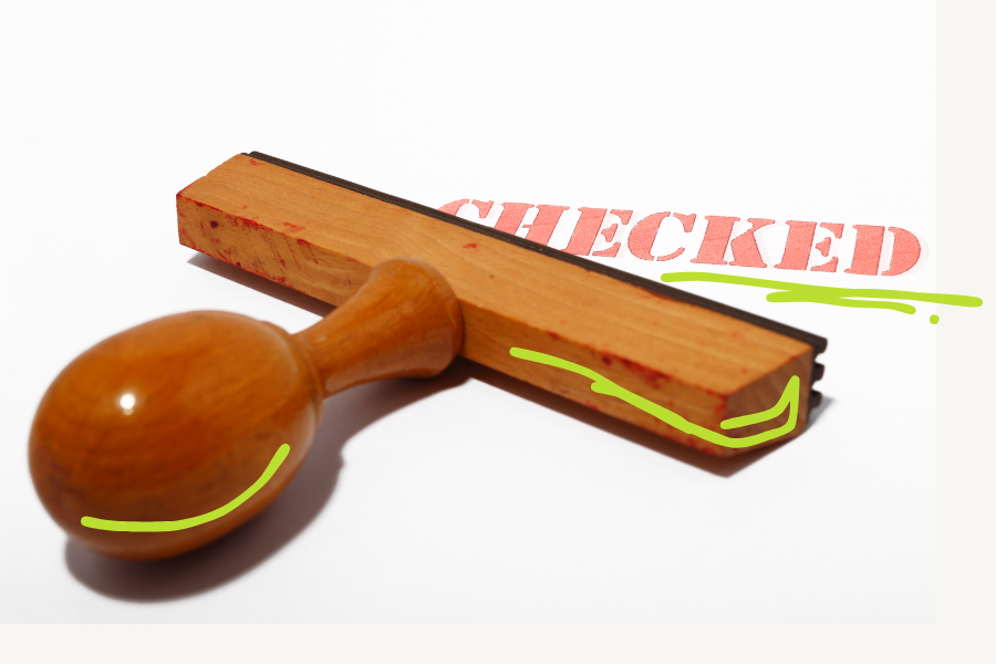 Wooden rubber stamp on white paper with a red imprint reading CHECKED, with green hand-drawn lines on the stamp and under the imprint, a symbol for checking off a rule and for ownership